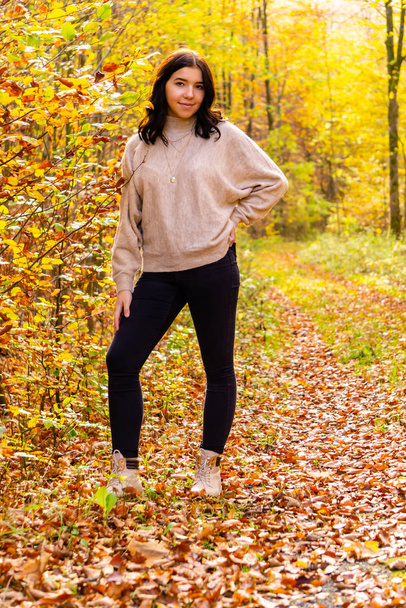 Молода дівчина з бежевим светром і чорними джинсами стоїть у барвистому осінньому лісі в жовтні в Баварії (Німеччина). - Фото, зображення