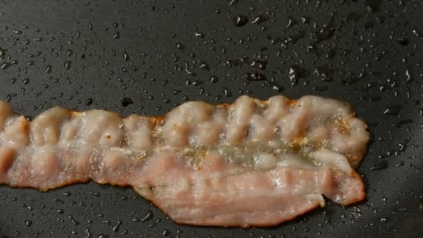 Una rebanada delgada de tocino se fríen en aceite de girasol en la sartén caliente con recubrimiento antiadherente de cerca ver
 - Metraje, vídeo
