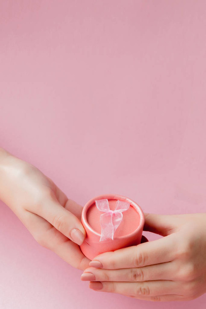 Round pink gift box in women's hands on a pink background. Festive concept for Valentine's day, Mother's day or birthday - Φωτογραφία, εικόνα