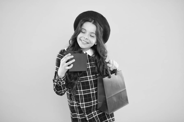 little shopaholic. kid fashion. happy girl in french beret. child with gift box on yellow background. small girl kid hold shopping bag. black friday. holiday presents by low price. best price - Photo, Image