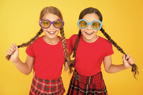 Summer accessory. Girls cute sisters similar outfits wear colorful sunglasses for summer season. Kids fashionable friends posing in sunglasses on yellow background. Summer fashion trend. Summer fun - Foto, Imagen