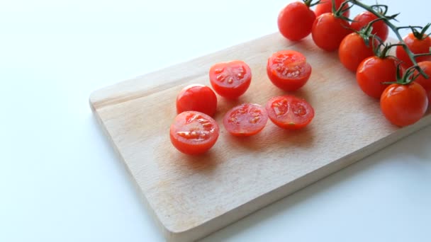 Ripe red small cherry tomatoes in a bunch of clusters and partially cut on the kitchen board and white background - Footage, Video