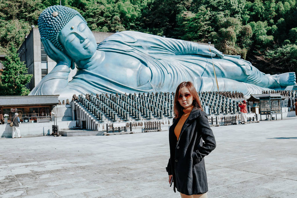 Urocza dziewczyna przed Wielkim Buddą w świątyni Nanzo-in, Fukuoka, Japonia. Nanzoin to świątynia buddyjska sekty Shingon w Sasaguri, prefektura Fukuoka, Japonia. - Zdjęcie, obraz