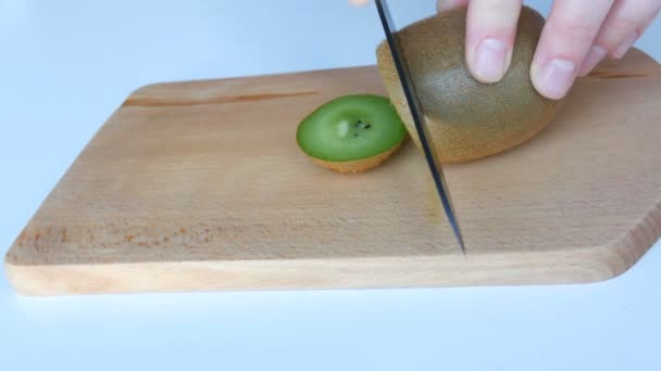 Ženské ruce střih zralé kiwi na kuchyňské dřevěné desce s černým keramickým nožem na bílém stole - Záběry, video