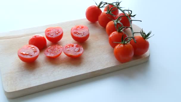 Dojrzałe czerwone małe pomidory wiśniowe w kilka klastrów i częściowo pocięte na tablicy kuchennej i białym tle - Materiał filmowy, wideo