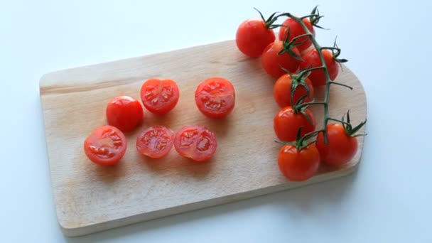 Bir demet küme içinde olgun kırmızı küçük domatesler ve mutfak tahtasında kısmen kesilmiş beyaz arka plan. - Video, Çekim
