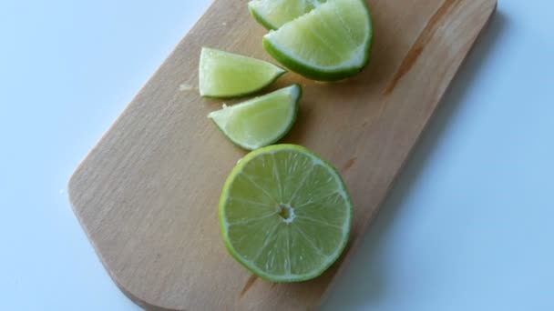 reife grüne Limette in Scheiben geschnitten auf Küchenholzbrett auf weißem Tischhintergrund - Filmmaterial, Video