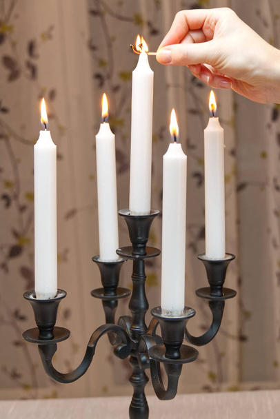 Kaarsen branden in retro kandelaar staat op tafel in de kamer. Een vrouw steekt kaarsen aan. Romantische sfeer. Zwarte kandelaar. Mooie decoratie. Oude of antieke stijl. - Foto, afbeelding