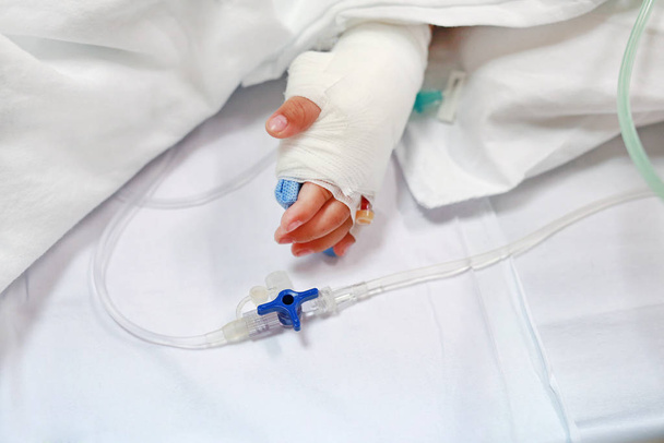 Close up baby hand on patient's bed in hospital with saline intravenous. Baby admitted at hospital. Kid patients have IV tube. - Photo, Image