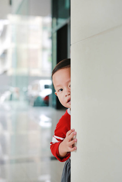 Adorable little boy hide behind a corner room. Baby playing peekaboo game indoor. - Fotó, kép
