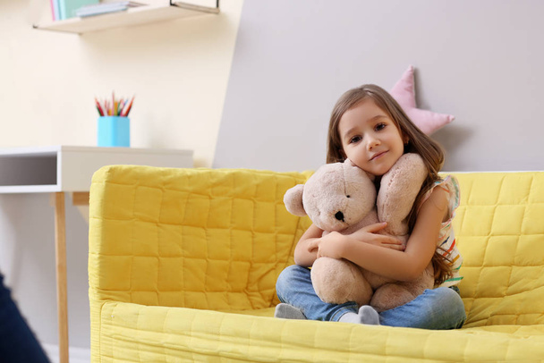 Cute little girl sitting on sofa at home - 写真・画像