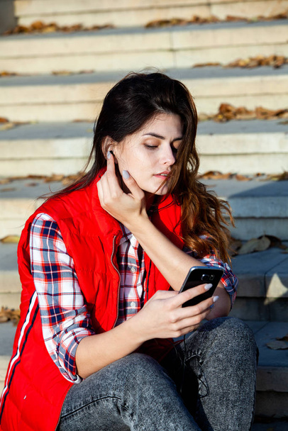 Kuva kaunis tyylikäs nainen tilalla matkapuhelin. Nuori eurooppalainen tyttö seisoo kadulla ja käyttää kännykkää. Nainen kuuntelee musiikkia puhelimen kanssa ja pitää hauskaa. Mobiili internet käsite. Sosiaalinen media
. - Valokuva, kuva