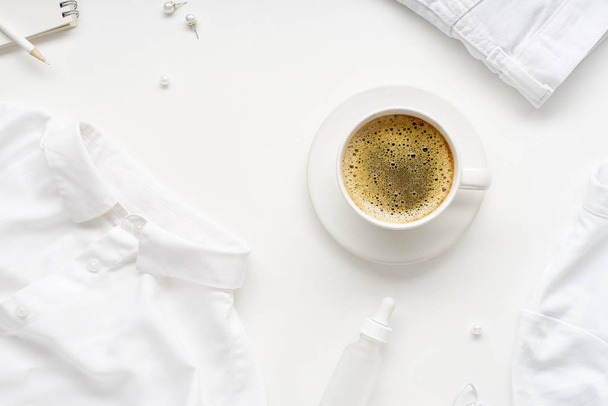 Creative flat lay with monochromatic white clothes and accessories with cup of coffee on white background. No stain concept                                - Фото, изображение