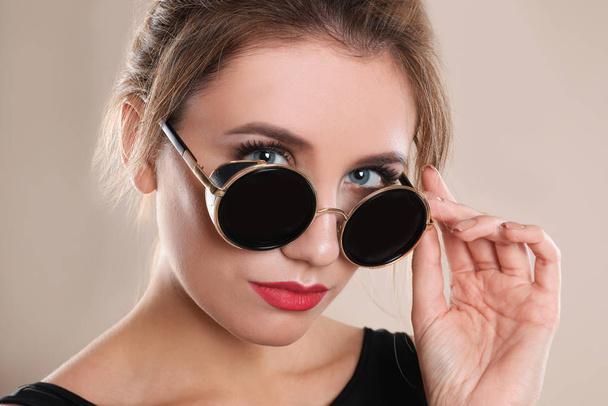 Young woman wearing stylish sunglasses on beige background - Foto, Imagem