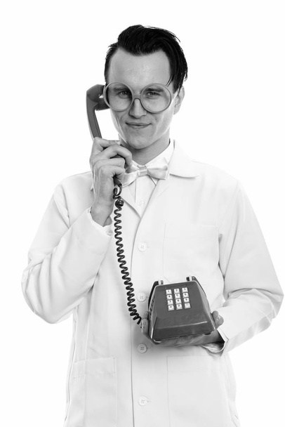 Studio shot of young crazy man doctor holding old telephone - Фото, изображение