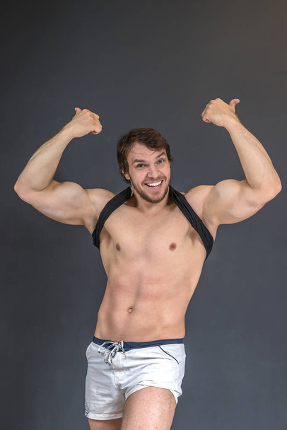 Muscular strong athletic bodybuilder or fitness model showing happy thumbs by two hands up gesture, smiling and posing near grey wall - Fotó, kép