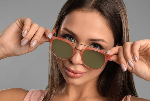Beautiful young woman wearing sunglasses on grey background, closeup - 写真・画像