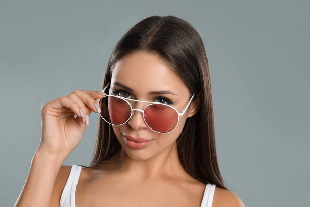 Beautiful young woman wearing sunglasses on grey background - Foto, afbeelding