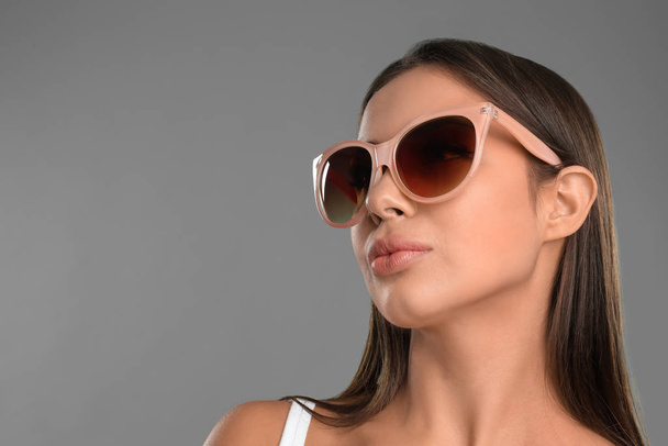Beautiful young woman wearing sunglasses on grey background. Space for text - Φωτογραφία, εικόνα