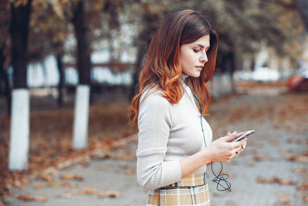 Изображение красивой стильной женщины с мобильным телефоном. Молодая европейская девушка стоит на улице и пользуется мобильным телефоном. Женщина слушает музыку по телефону и веселится. Концепция мобильного интернета Социальные сети
. - Фото, изображение