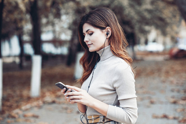Зображення красивої стилізованої жінки, що тримає мобільний телефон. Молода європея стоїть на вулиці і користується мобільним телефоном. Жінка слухає музику по телефону і розважається. Концепція мобільного інтернету. Соціальні медіа. - Фото, зображення