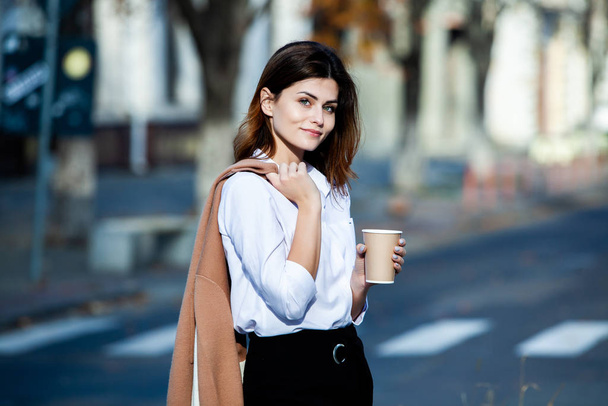 Young stylish woman drinking tea in a city street. Hipster european girl with latte paper glass  in street. Gorgeous young woman with cup of coffee in city street. Coffee break. Coffee to go.  - Foto, Imagem