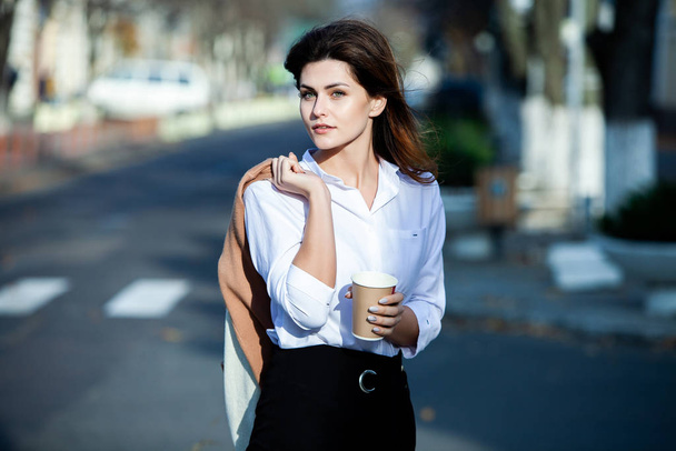 Young stylish woman drinking tea in a city street. Hipster european girl with latte paper glass  in street. Gorgeous young woman with cup of coffee in city street. Coffee break. Coffee to go.  - Zdjęcie, obraz