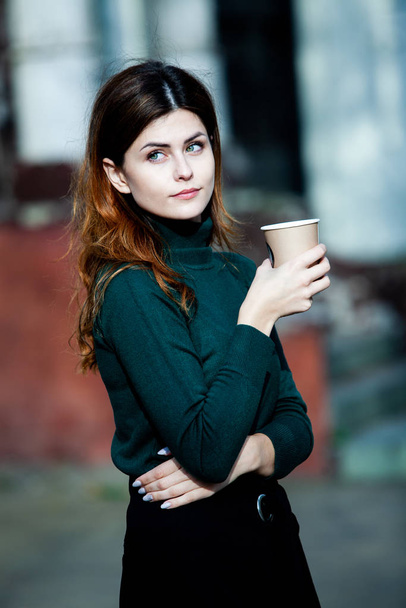 Fiatal, stílusos nő teát iszik egy városi utcában. Hipster európai lány latte papírpohárral az utcán. Gyönyörű fiatal nő egy csésze kávéval a város utcájában. Kávészünet. Kávét elvitelre..  - Fotó, kép