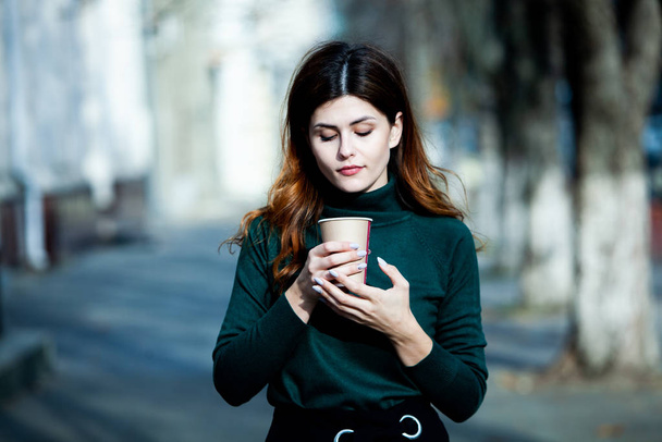Młoda stylowa kobieta pijąca herbatę na ulicy. Hipsterska Europejka ze szklanką papieru latte na ulicy. Wspaniała młoda kobieta z filiżanką kawy na ulicy. Przerwa na kawę. Kawa na wynos.  - Zdjęcie, obraz