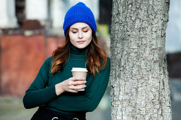 Giovane donna elegante bere il tè in una strada della città. Ragazza europea hipster con vetro di carta latte in strada. Splendida giovane donna con una tazza di caffè in strada. Pausa caffè. Caffè da portare via
.  - Foto, immagini