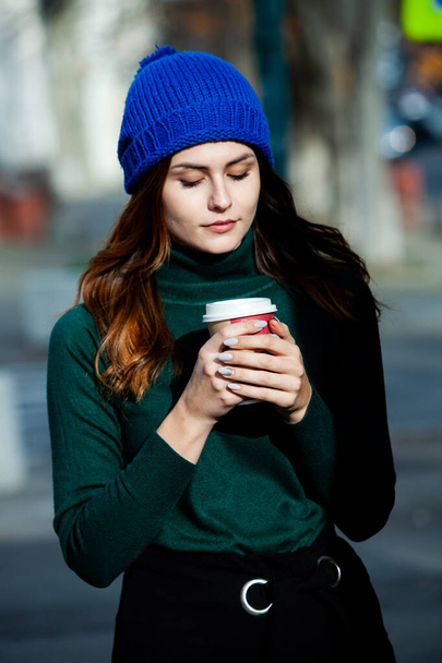 Młoda stylowa kobieta pijąca herbatę na ulicy. Hipsterska Europejka ze szklanką papieru latte na ulicy. Wspaniała młoda kobieta z filiżanką kawy na ulicy. Przerwa na kawę. Kawa na wynos.  - Zdjęcie, obraz