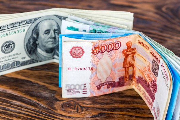 egy két köteg orosz rubel és egy dollár bankjegy barna fa felületen, szelektív fókusszal. - Fotó, kép
