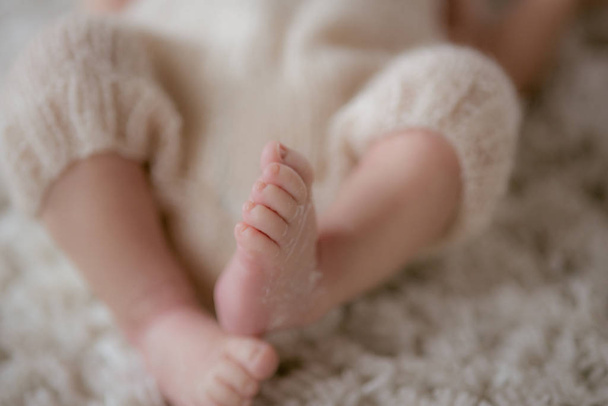 Little cute legs of a baby who lies in a wicker basket with knitted plaids at home. Happy motherhood - Foto, Imagem