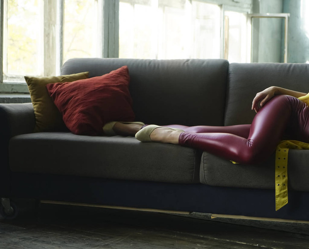 detail of woman wearing red leather  pants and  white low shoe. female lie on gray coach, sofa with two pilliows. open window. sunny day. no face. - Foto, Bild