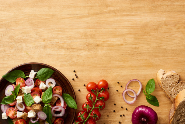 Lezzetli İtalyan sebze salatası panzanella tabakta taze malzemelerin yanında, ahşap masada servis ediliyor. - Fotoğraf, Görsel