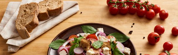 delicious Italian vegetable salad panzanella served on plate on wooden table near tomatoes and bread, panoramic shot - Fotoğraf, Görsel