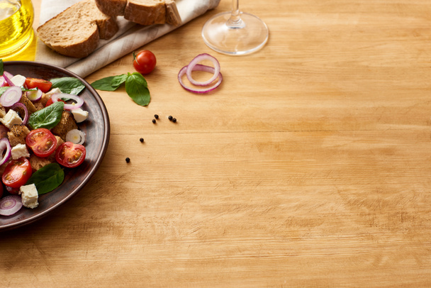 ízletes olasz zöldségsaláta panzanella tálcán tálalva fa asztalon friss összetevők közelében - Fotó, kép