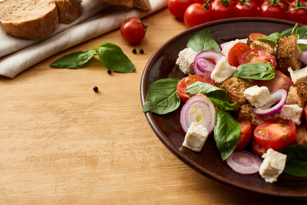 delicious Italian vegetable salad panzanella served on plate on wooden table near fresh ingredients and bread - Photo, image