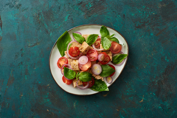 bovenaanzicht van heerlijke Italiaanse groentesalade panzanella geserveerd op plaat op getextureerd groen oppervlak - Foto, afbeelding