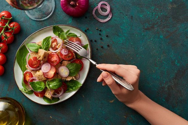 cropped view of woman eating delicious Italian vegetable salad panzanella on textured green surface with ingredients - Foto, Imagen