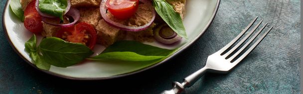 közeli kilátás ízletes olasz zöldségsaláta panzanella tálalva tányéron texturált zöld felületen villával, panorámás lövés - Fotó, kép