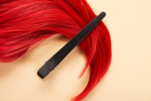 Top view of clip and colored red hair on beige background - Foto, imagen