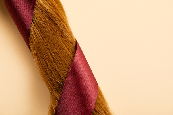Top view of burgundy ribbon on brown hair on beige background - Foto, imagen