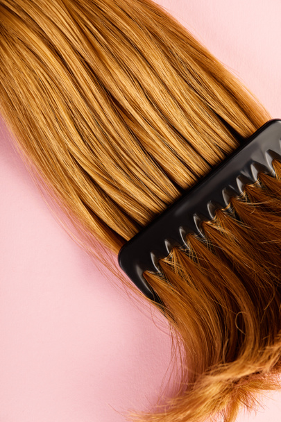 Top view of brown hair and comb on pink background - Foto, afbeelding