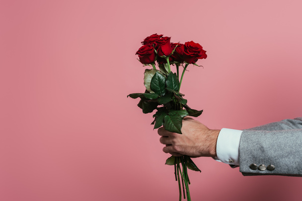 przycięty widok człowieka gospodarstwa bukiet czerwonych róż, izolowane na różowy - Zdjęcie, obraz