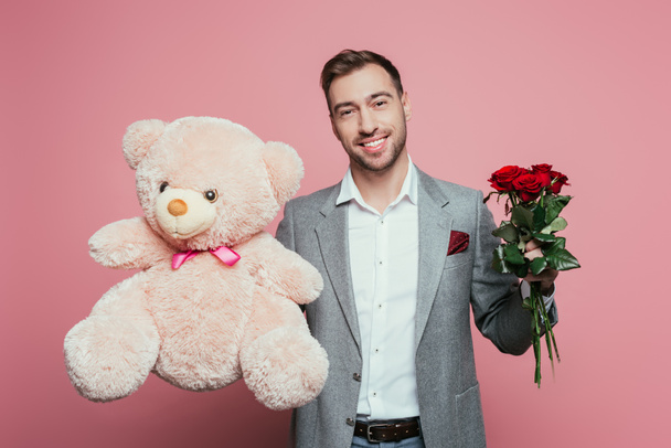 smiling man holding teddy bear and roses, isolated on pink - Valokuva, kuva