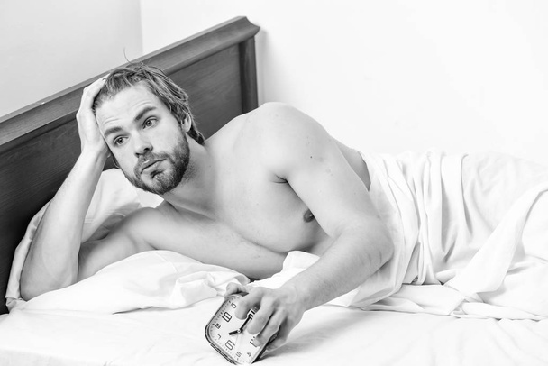 Handsome man using clock in bed after waking up in the morning. Cheerful young man is waking up after sleeping in the morning. Male in the house. - Foto, Imagen