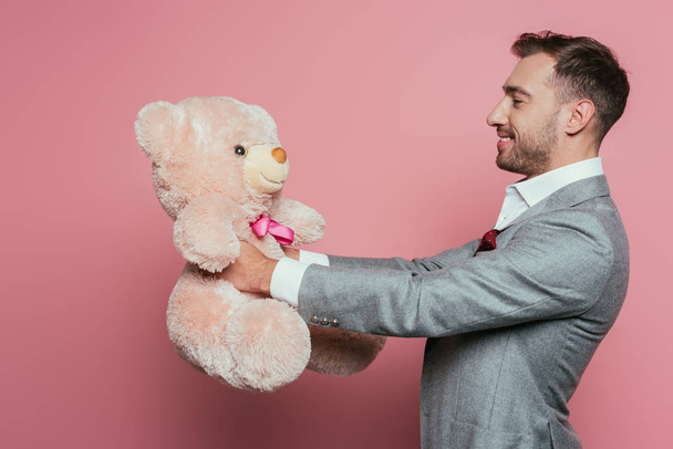 cheerful man in suit holding teddy bear on pink - Φωτογραφία, εικόνα