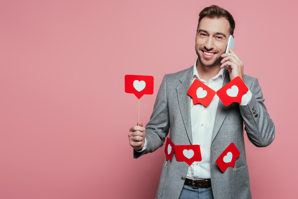 cheerful man talking on smartphone and holding cards with hearts for valentines day, isolated on pink  - Fotografie, Obrázek