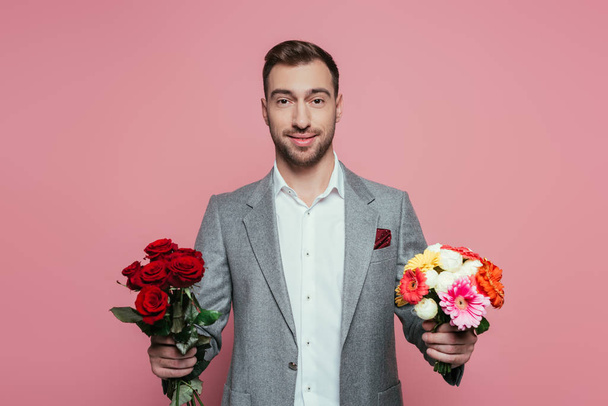 parrakas hymyilevä mies puku tilalla kaksi kukkakimppuja, eristetty vaaleanpunainen
 - Valokuva, kuva